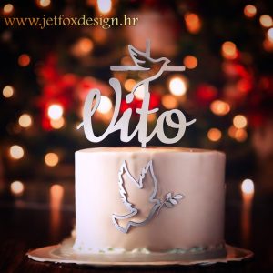 Tortni ukras s motivima križa i golubice, s dodatkom personaliziranog imena kao poseban detalj.