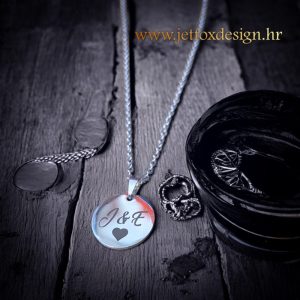 Personalizirana ogrlica s okruglim privjeskom i graviranim inicijalima, ukrašena malim srcem – savršen simbol ljubavi i povezanosti.
