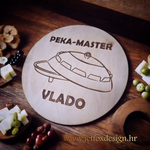 Okrugla drvena daska s gravurom peke i natpisom "Peka majstor", savršena za ljubitelje domaće spize i otvorene vatre.