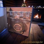 Pijani registrator s drveno ugraviranom bocom i čašicama, postavljen u blagdanskom okruženju s kaminom i borom.